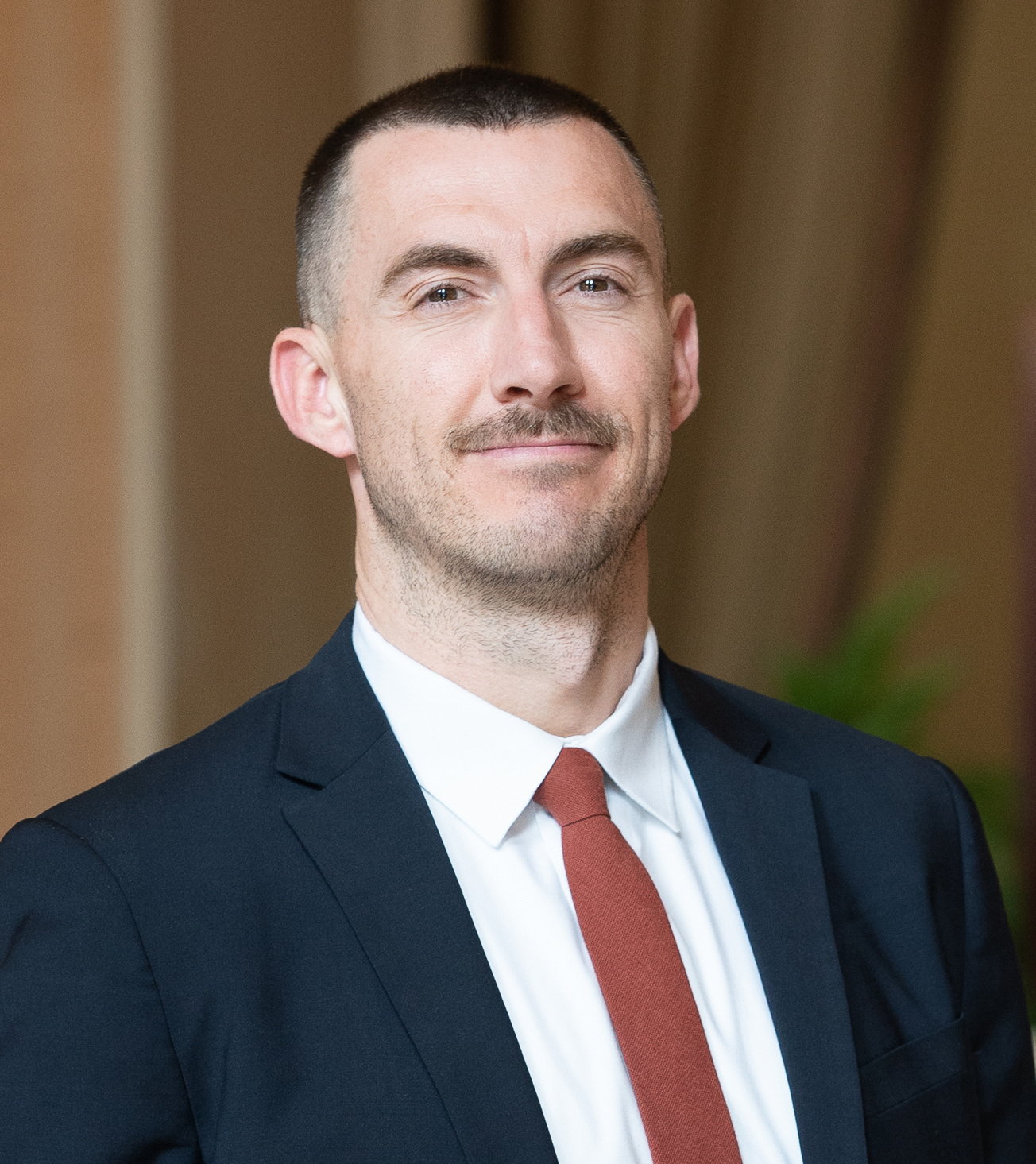 A photo of Craig Pulsipher wearing a navy blue blazer, white shirt, and red tie